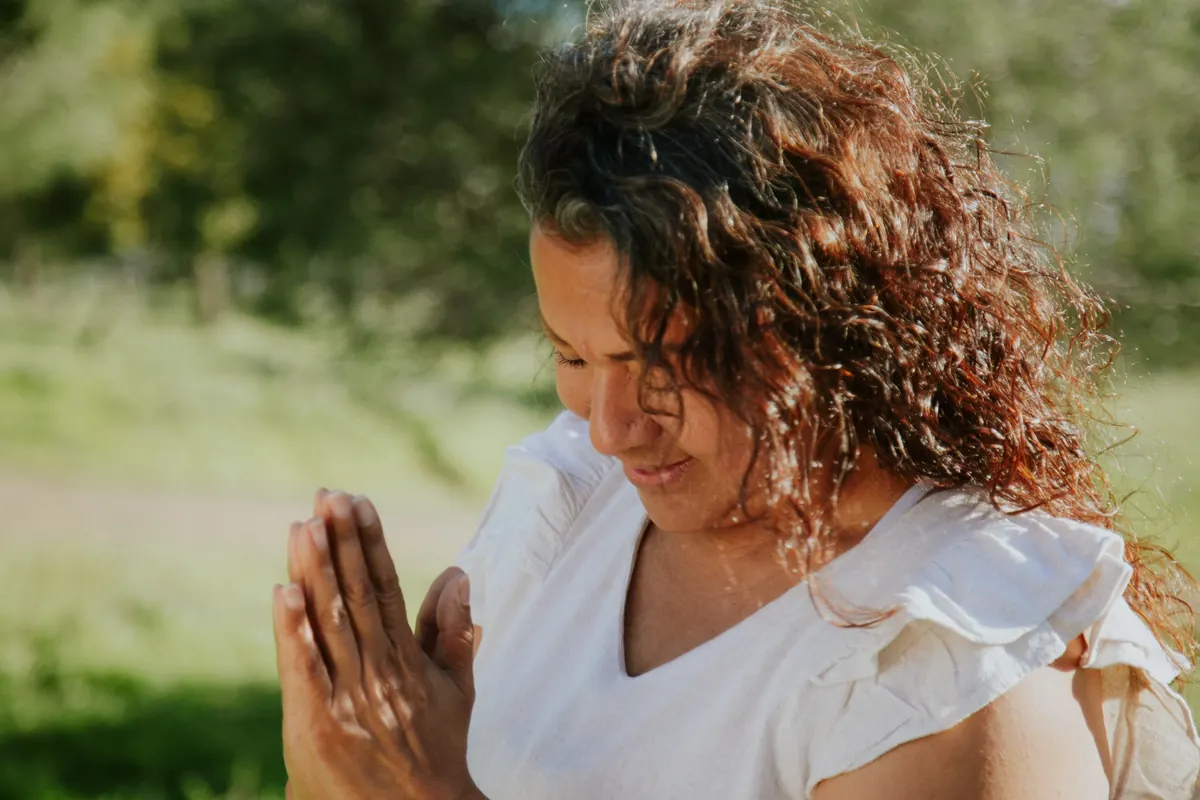 Mujer con las manos en oración en un jardín, recibiendo la luz del sol
